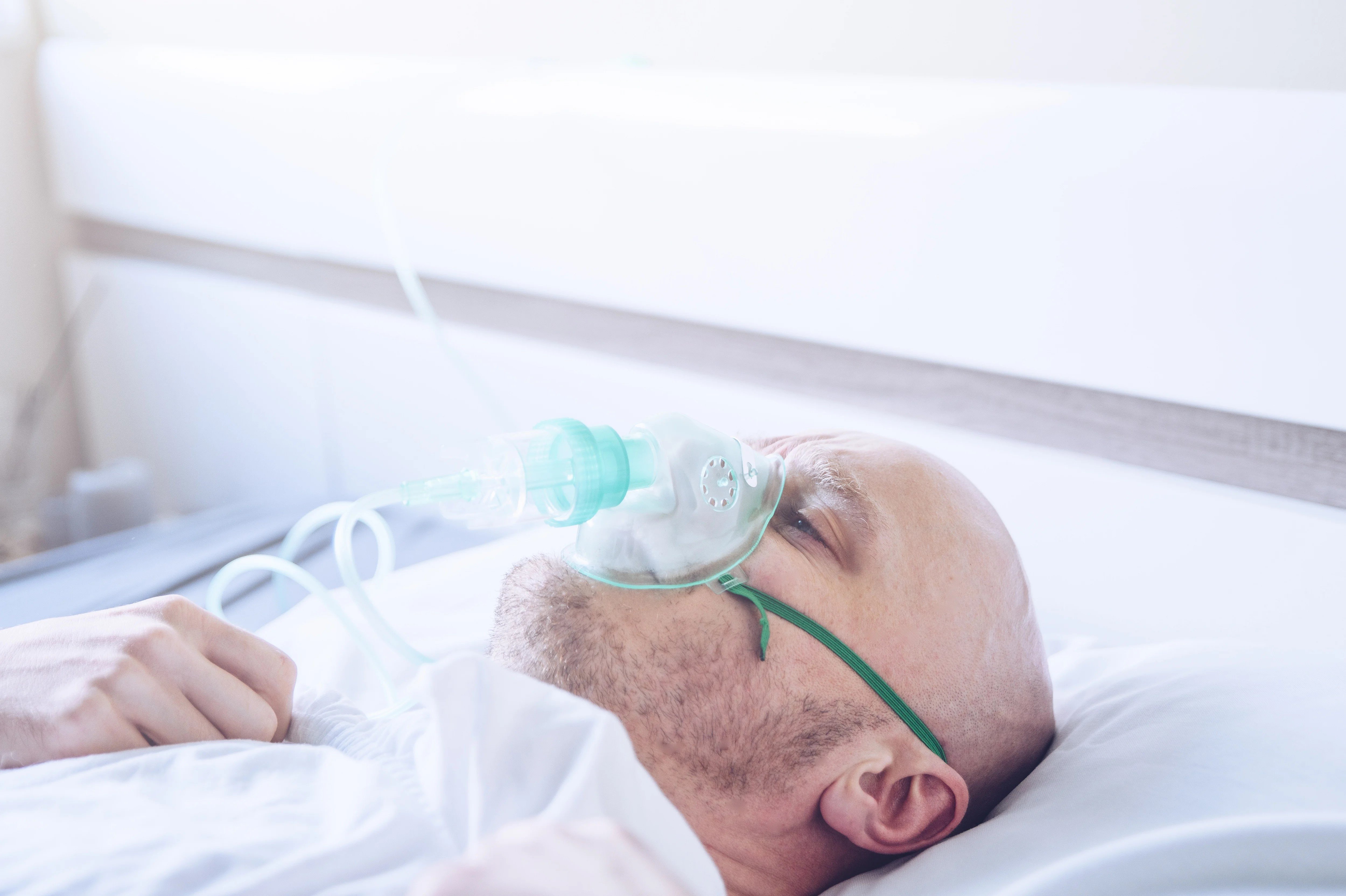 Image of a man laying in a hospital bed wearing an oxygen mask