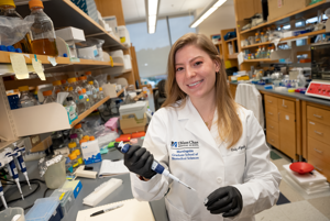 A woman in a research lab wearing a lab coat pipetting into a small tube