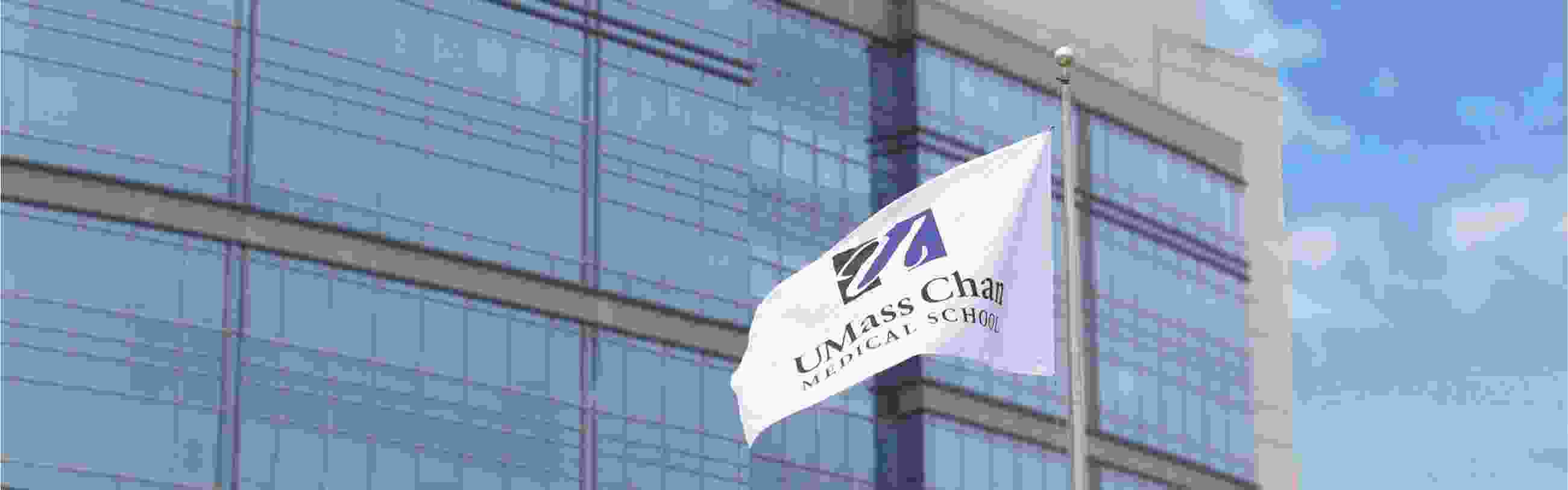 White flag bearing the UMass Chan Medical School name and logo flies in front of a building