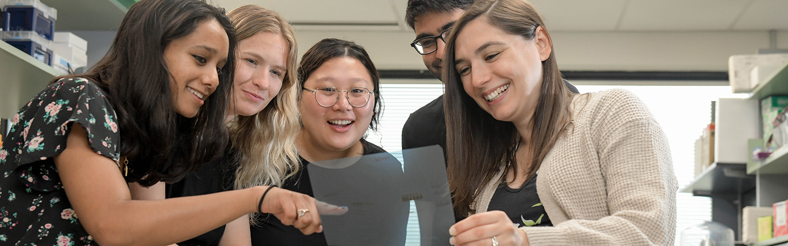 Professor looking over slides in a lab alongside student researchers