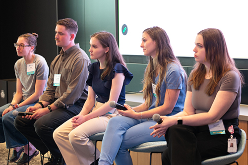 Panel of students sitting down looking toward audience.