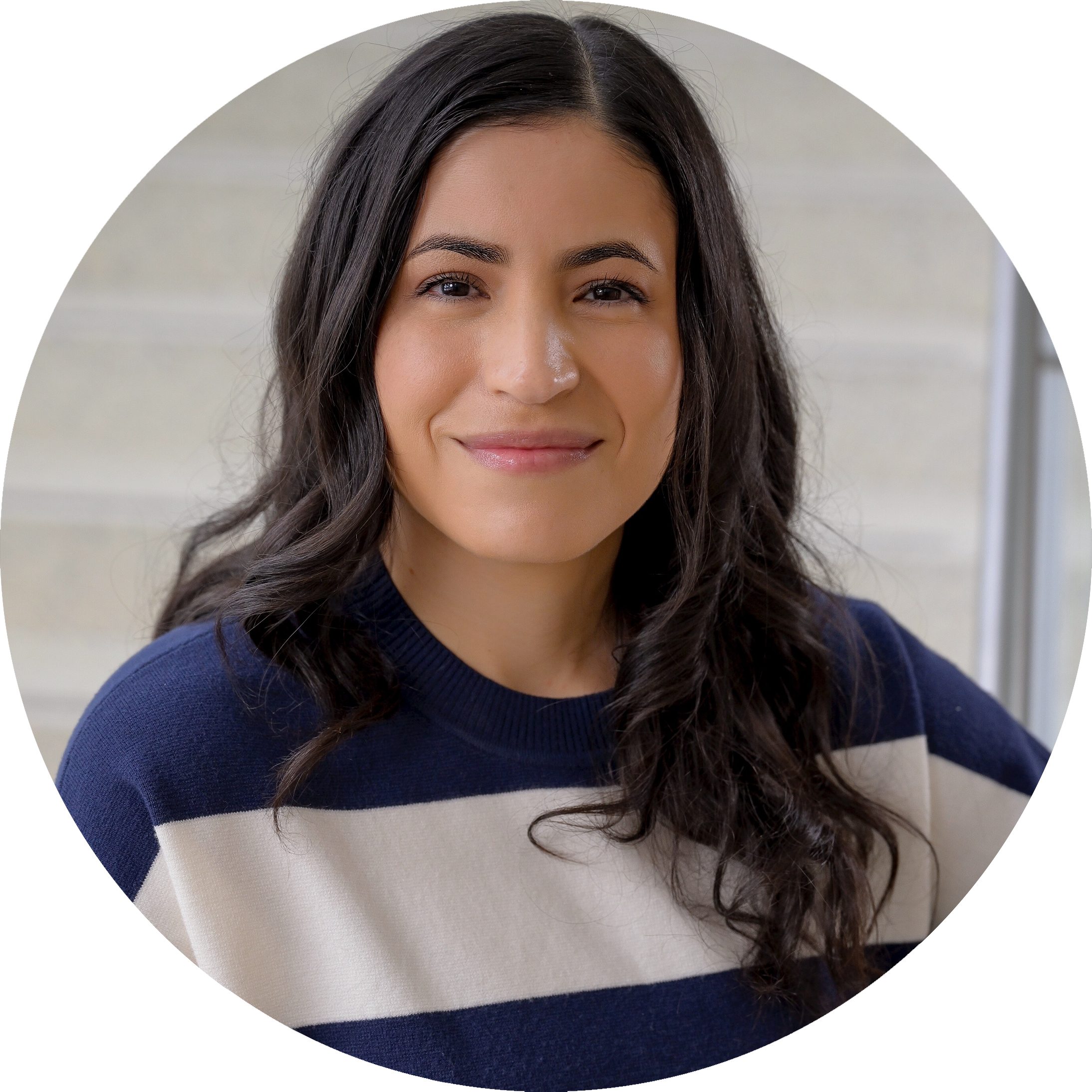 A headshot of Jennifer Vega with long dark hair in a navy and white striped sweater, smiling softly in front of a light-colored staircase