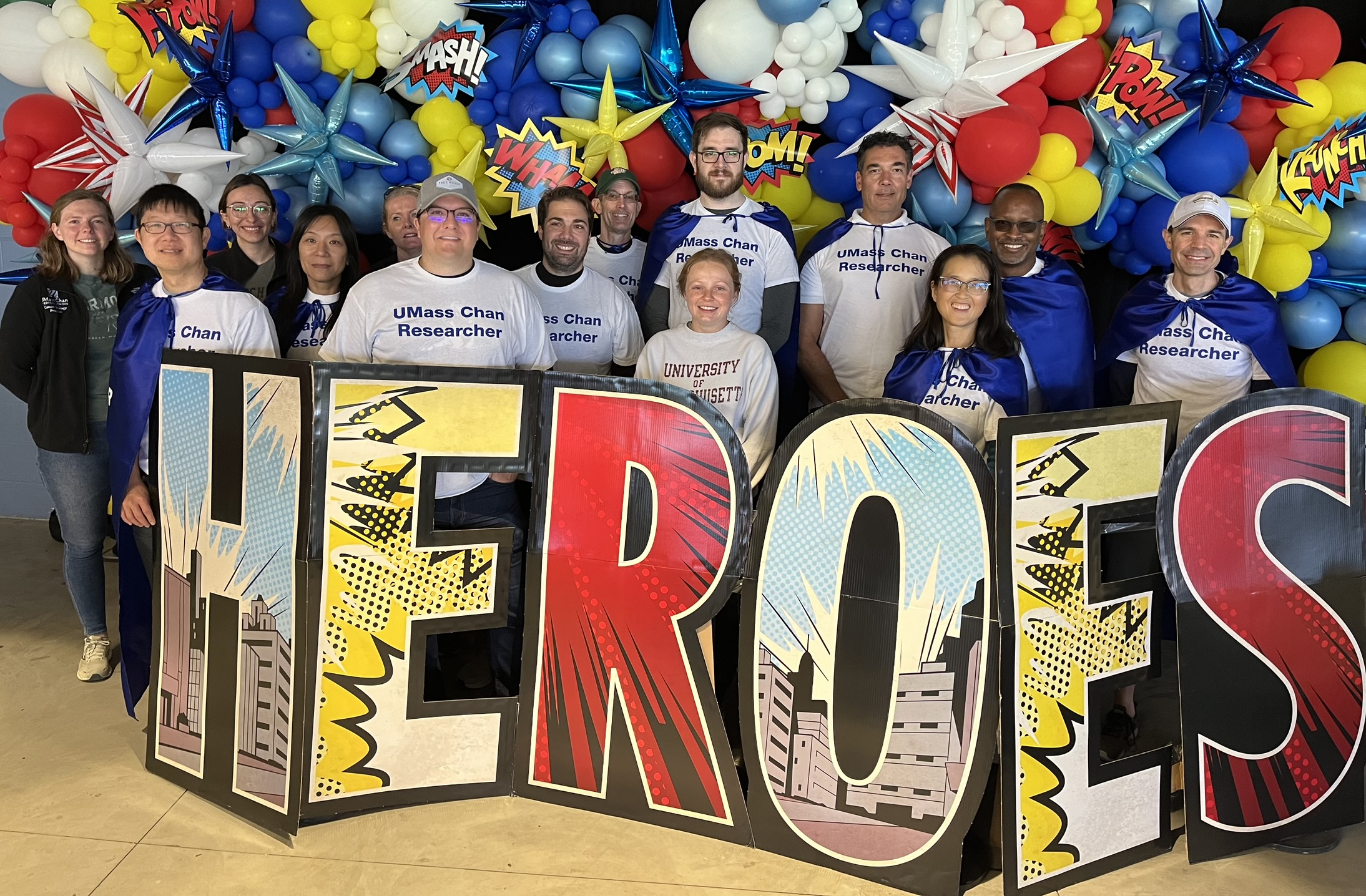 Group photo of the UMass Chan Cancer Research Team taken in 2024, standing behind a sign saying Heroes..