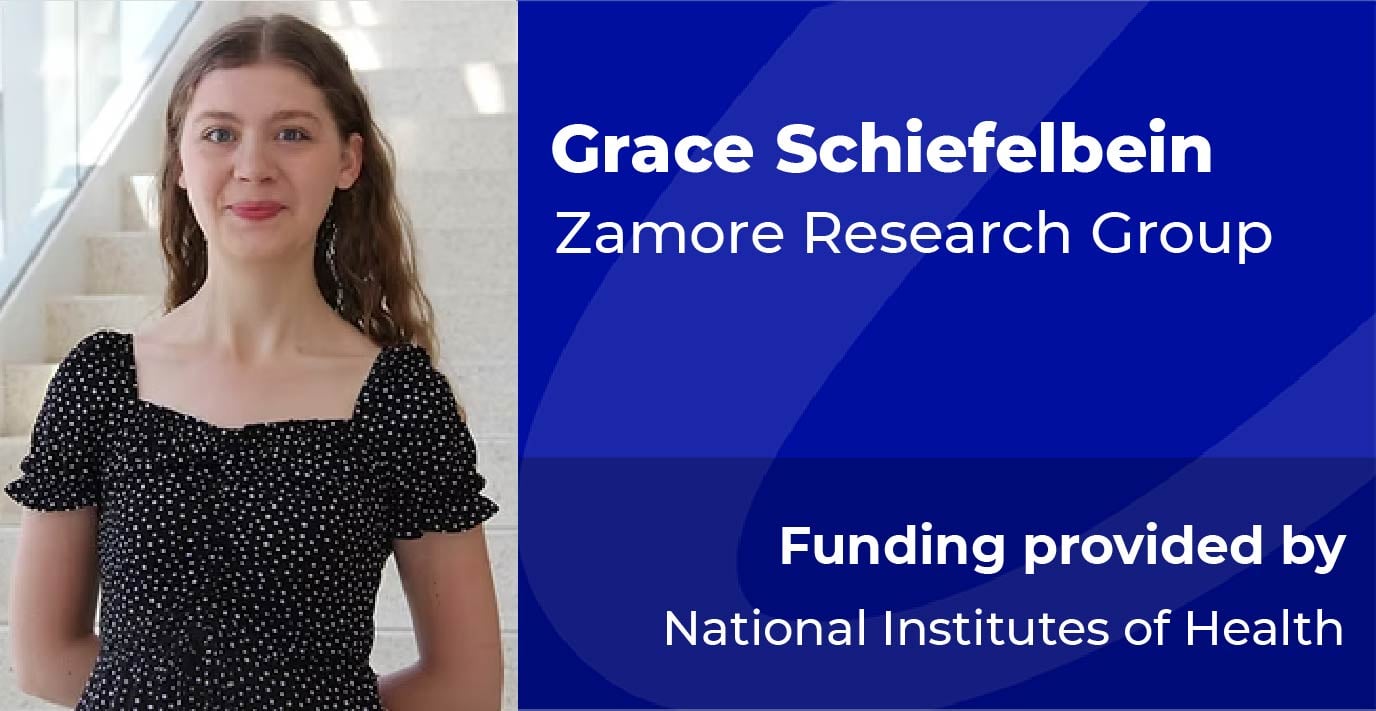 A researcher stands beside a blue information panel displaying the text: “Grace Schiefelbein, Zamore Research Group. Funding provided by National Institutes of Health.”