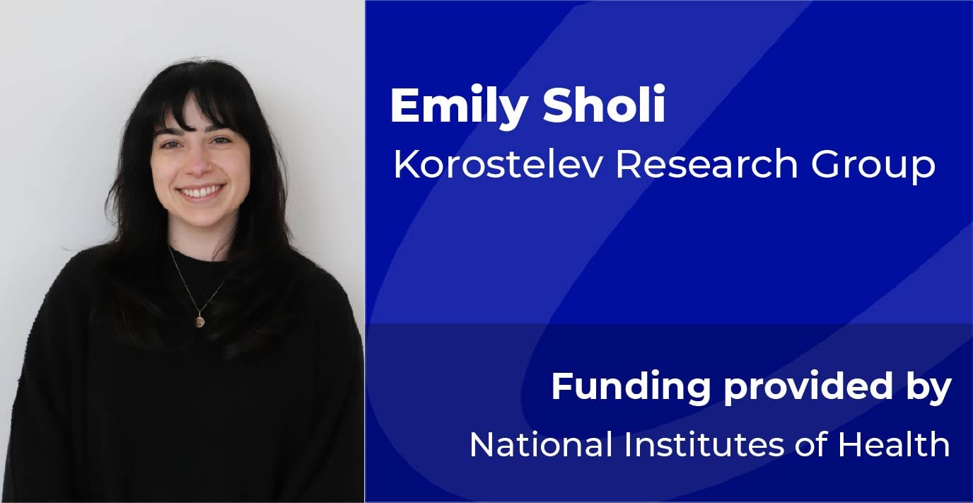 A researcher stands beside a blue information panel displaying the text: “Emily Sholi, Korostelev Research Group. Funding provided by National Institutes of Health.”