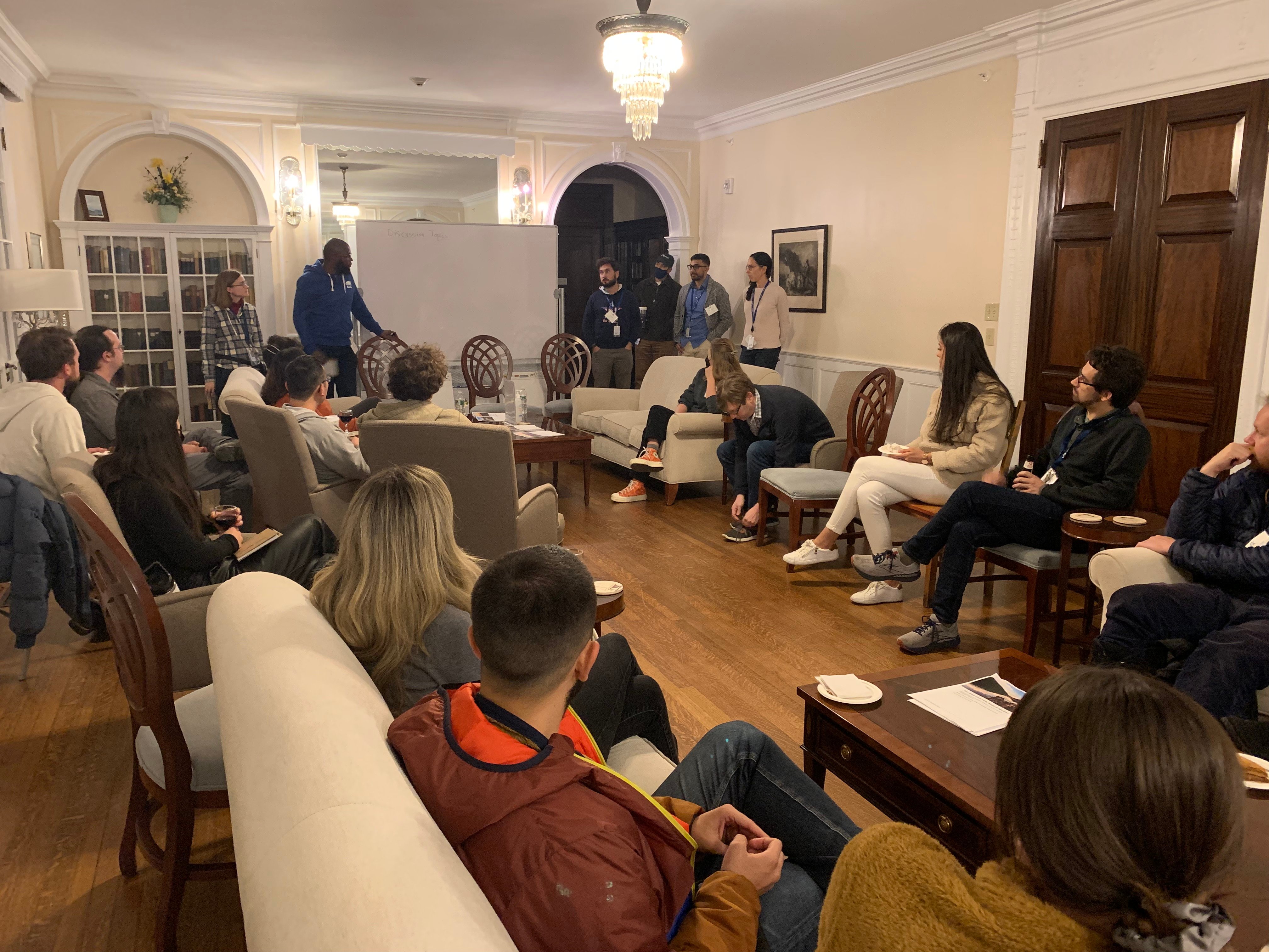 Panelists stand at the front of the room while a group of people watch attentively