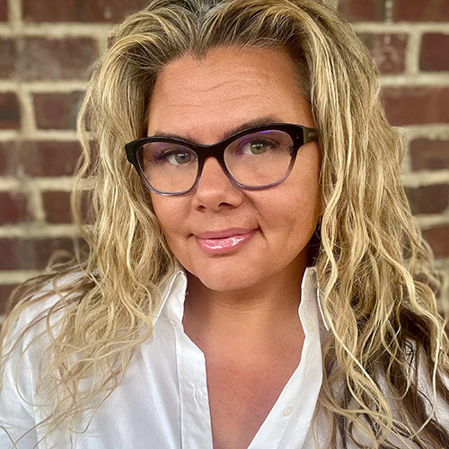 white woman with long blonde wavy hair and glasses