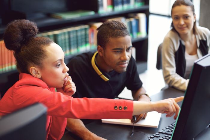 students in a college library looking at a computer screen