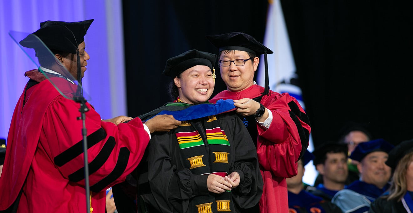 UMass Chan's student representative on the University of Massachusetts Board of Trustees, Bethany Berry (center), MD/PhD, is hooded during Sunday&rsquo;s Commencement ceremony