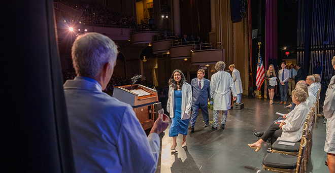 Medical students receive their white coats on stage with mentors and a person of their choosing.