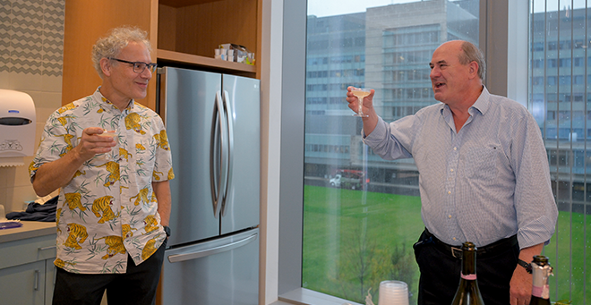 Ambros chats with Roger Davis, both holding champagne glasses